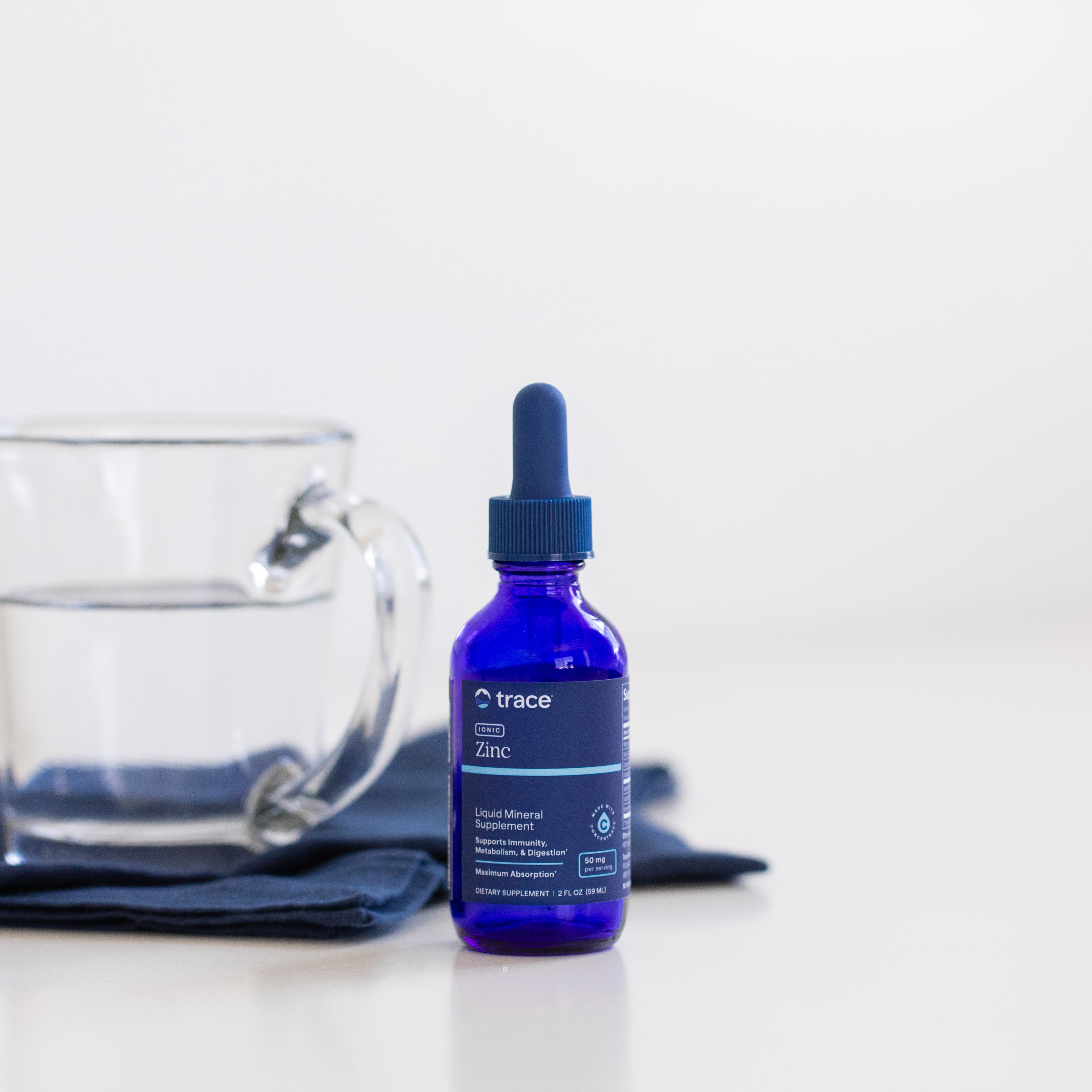 Trace minerals biotino ir kolageno pakuotė ant stalo, o antrame plane - stiklinė vandens