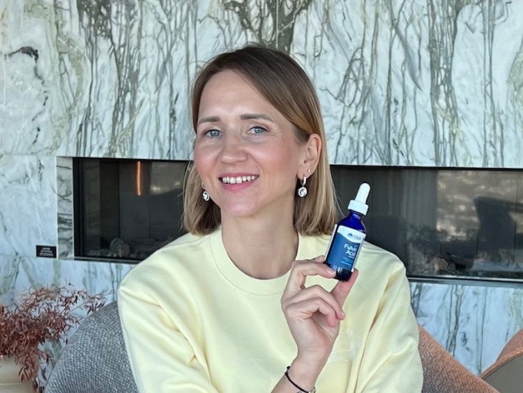 Moteris rankoje laiko Trace Minerals fulvinės rūgšties pakuotę ir šypsosi