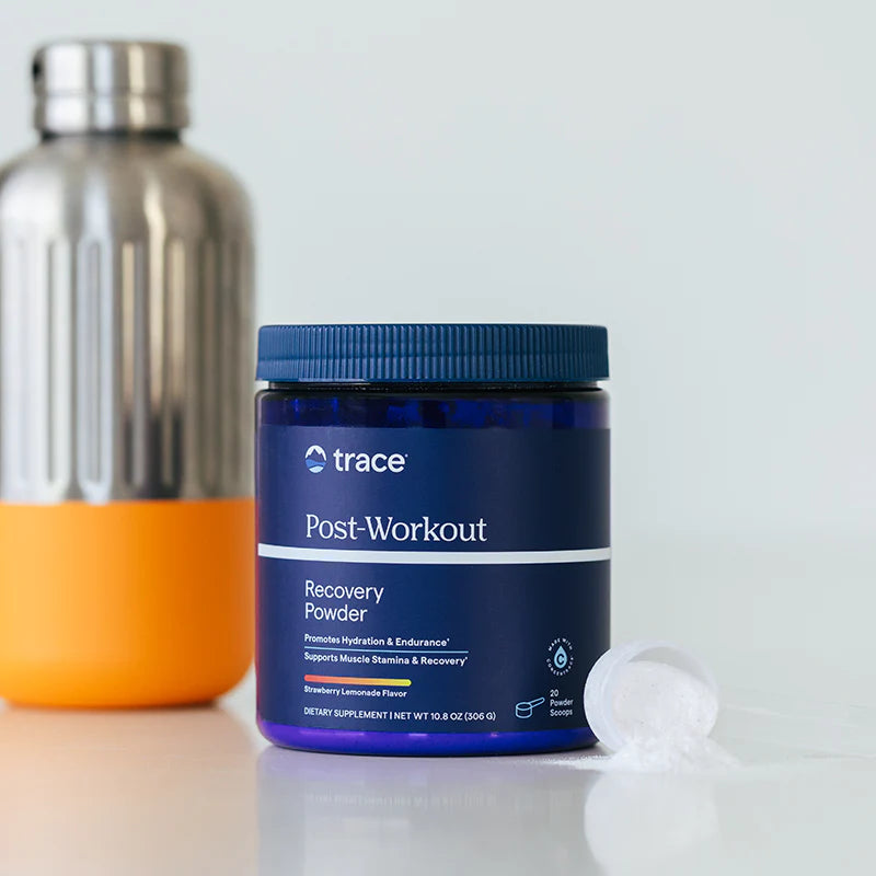 Trace Minerals Post Workout maisto papildo mėlyna pakuotė šviesiame fone, antrame plane gertuvė.