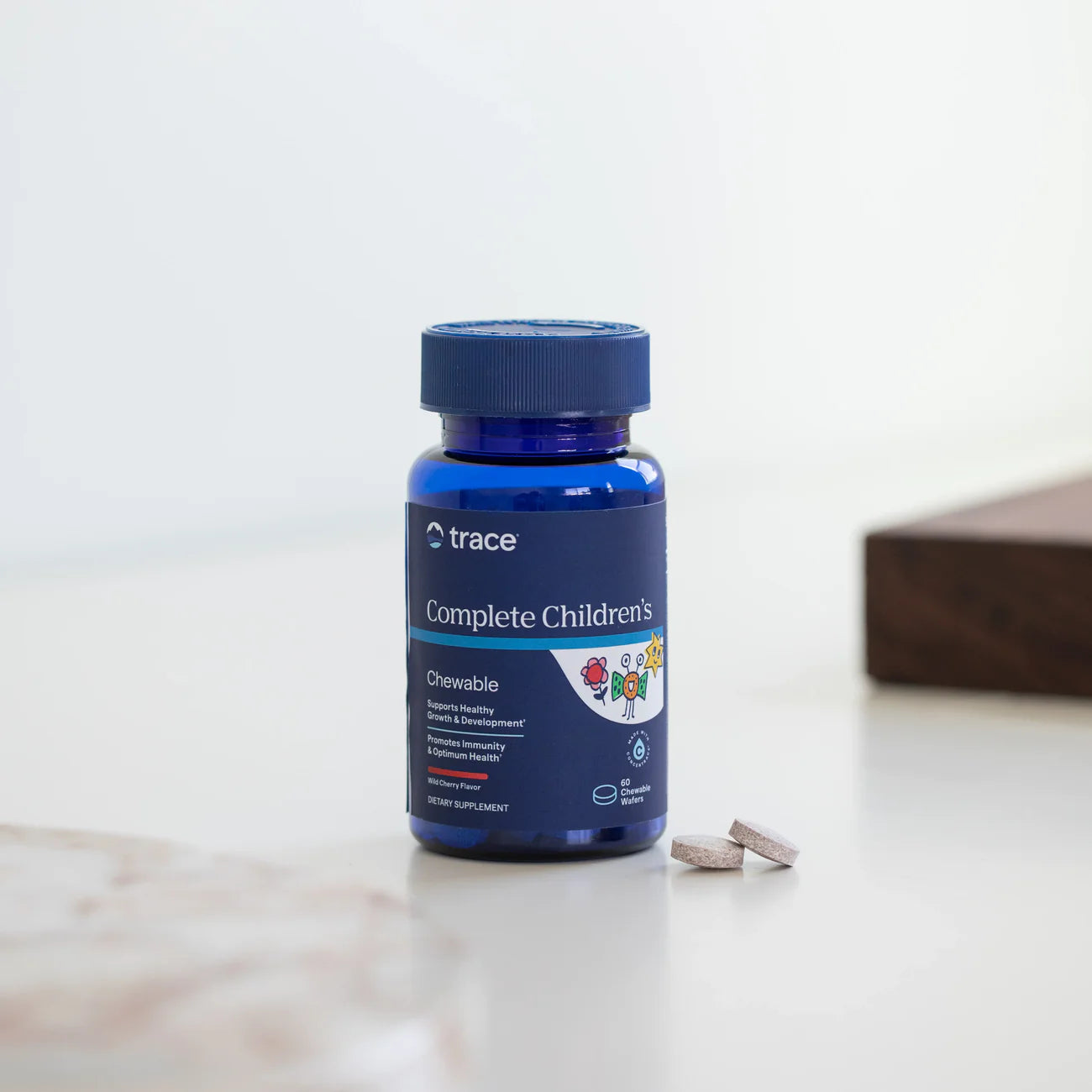 Trace Minerals kramtomų vitaminų vaikams ant stalo šviesiame fone su tabletėmis šalia