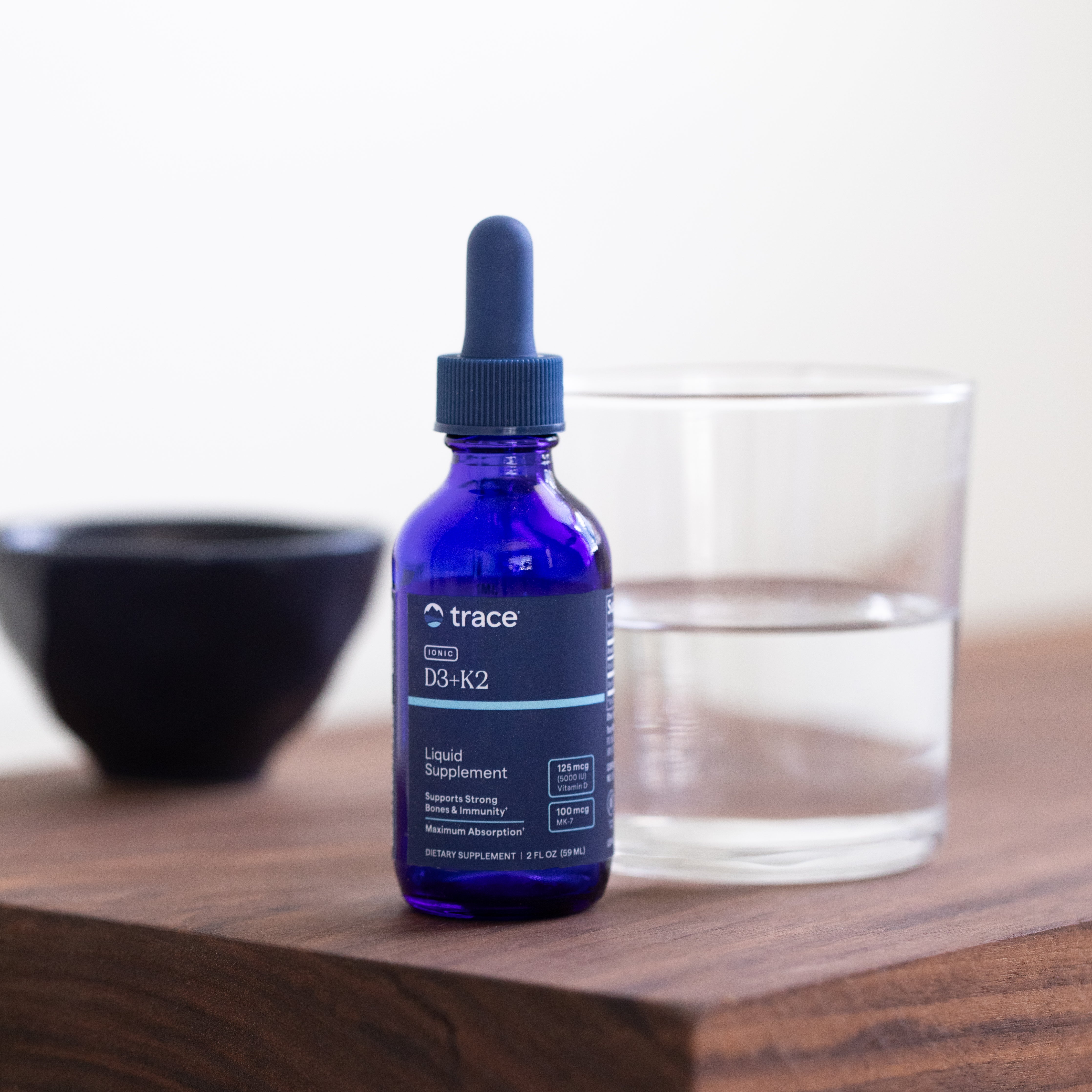 Trace Minerals vitamino D3+K2 pakuotė šviesiame fone ant stalo priešais stikline vandens